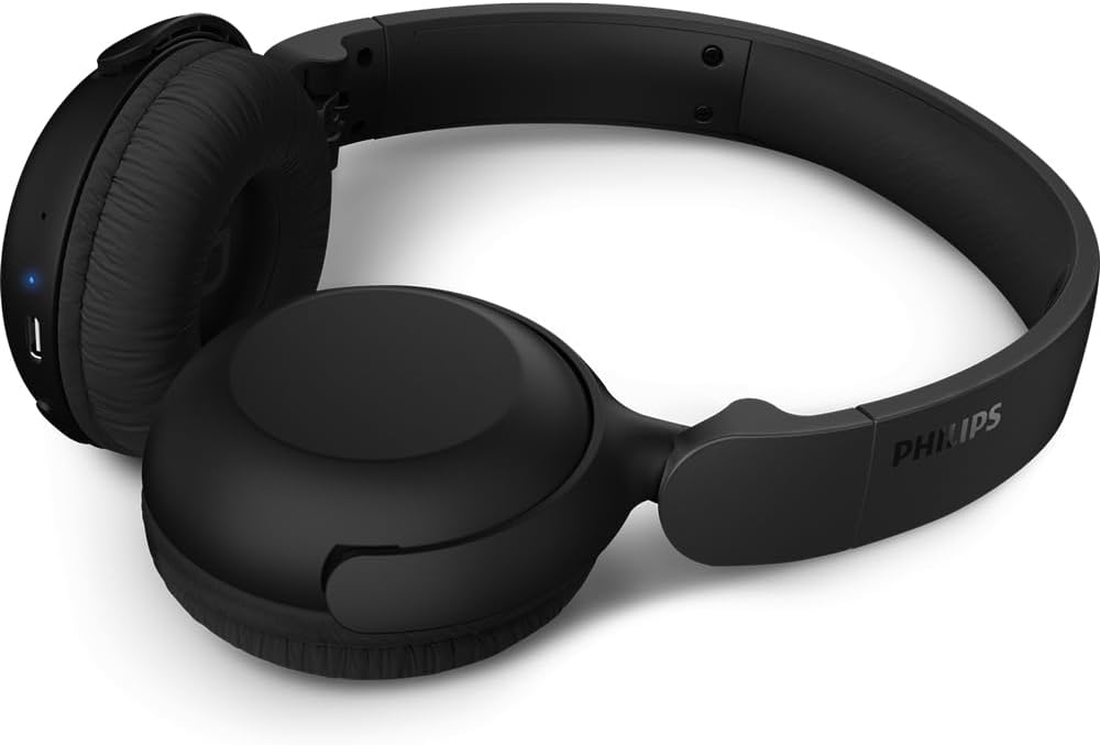 Fone de ouvido Philips TAH2209 Bluetooth Over-ear preto, posicionado de lado sobre superfície branca com botões de controle visíveis.