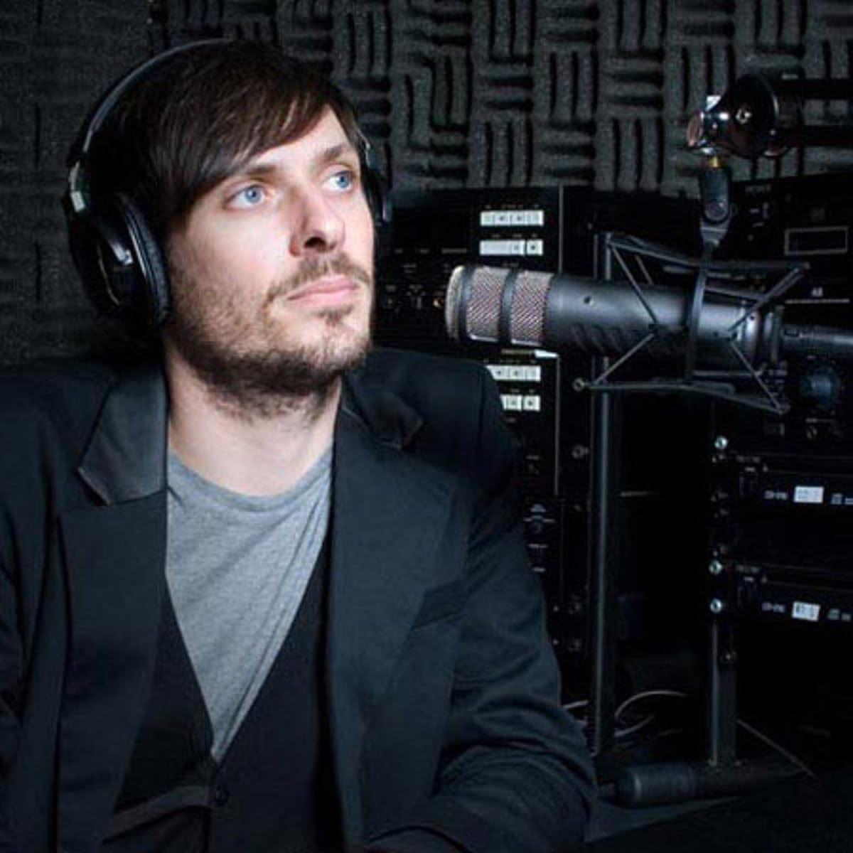 Homem usando fones de ouvido grandes pretos, sentado em estúdio com microfone profissional RØDE Procaster montado em suporte