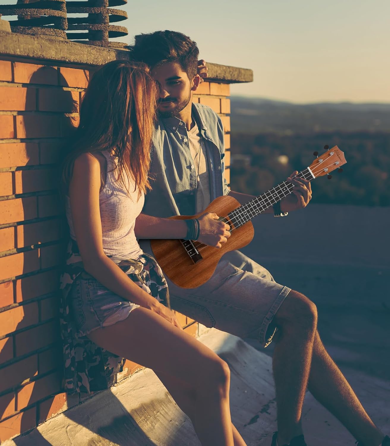 Casal jovem ao pôr do sol com o homem tocando ukulele Ulumac de mogno sólido em ambiente ao ar livre.
