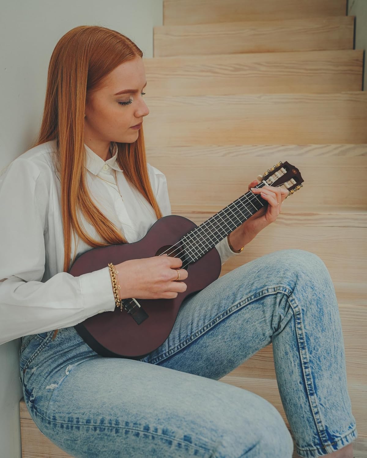 Mulher jovem tocando o guitalele Yamaha GL-1 sentada em escada de madeira