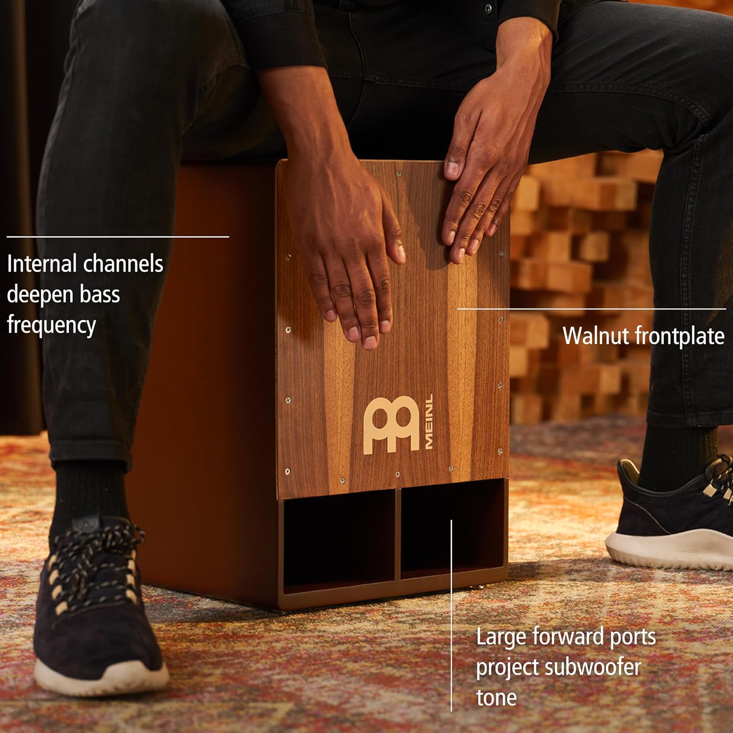 Homem sentado tocando o cajon Meinl Jumbo Bass Subwoofer com superfície de nogueira, destacando características do produto